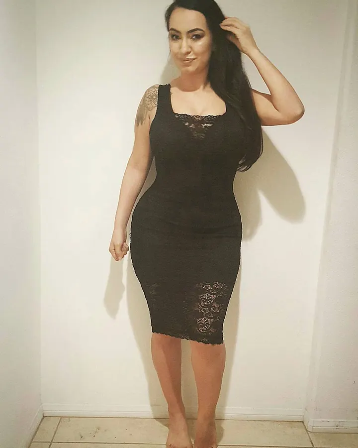 Femme arabe en robe noire ajustée, main dans les cheveux, regardant l'objectif.