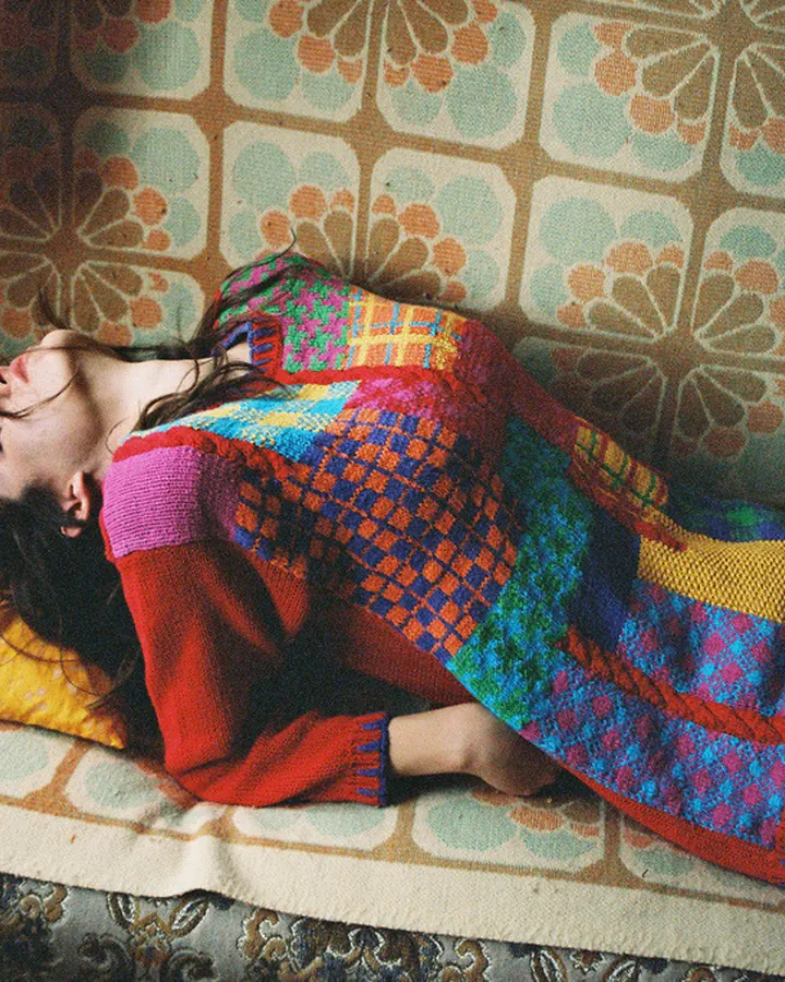 Femme arabe allongée sur un canapé coloré, portant un pull multicolore et un jean bleu.