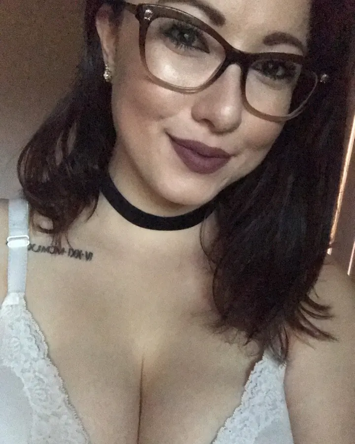 Femme aux cheveux bruns portant un soutien-gorge blanc, prenant un selfie, lunettes et collier noir